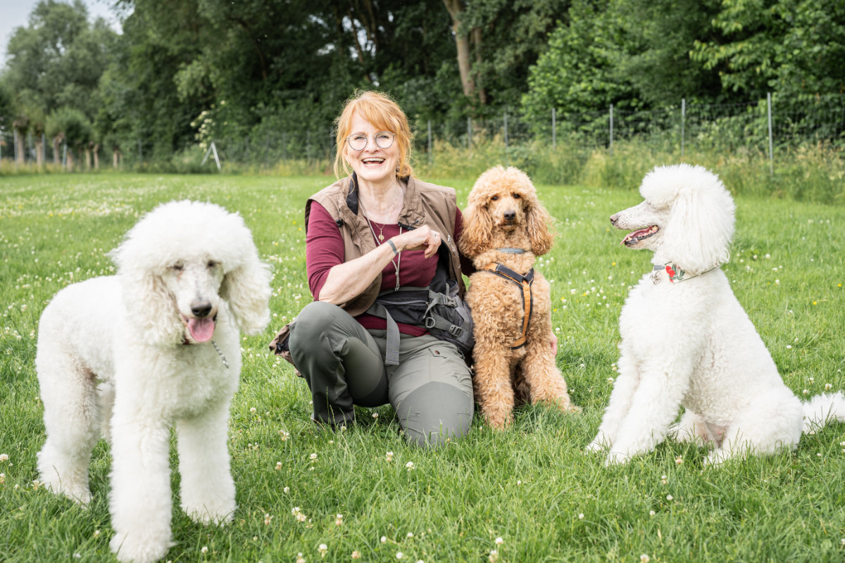 Hundetrainerin Regina Gadesmann kniet mit ihren drei Pudeln auf dem Trainingsgelände der Hundeschule Alfeld.