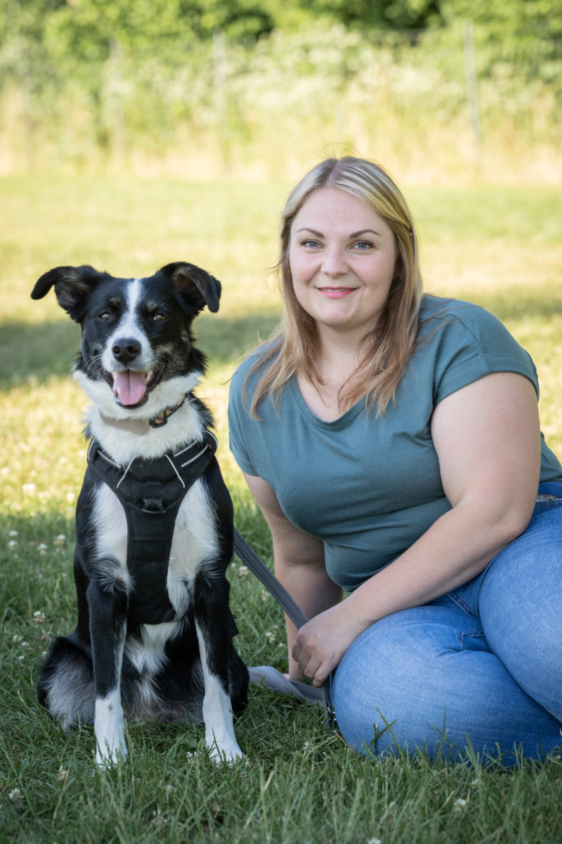 Eine zufriedene Teilnehmerin sitzt im Gras neben ihrem aufmerksamen Border Collie.