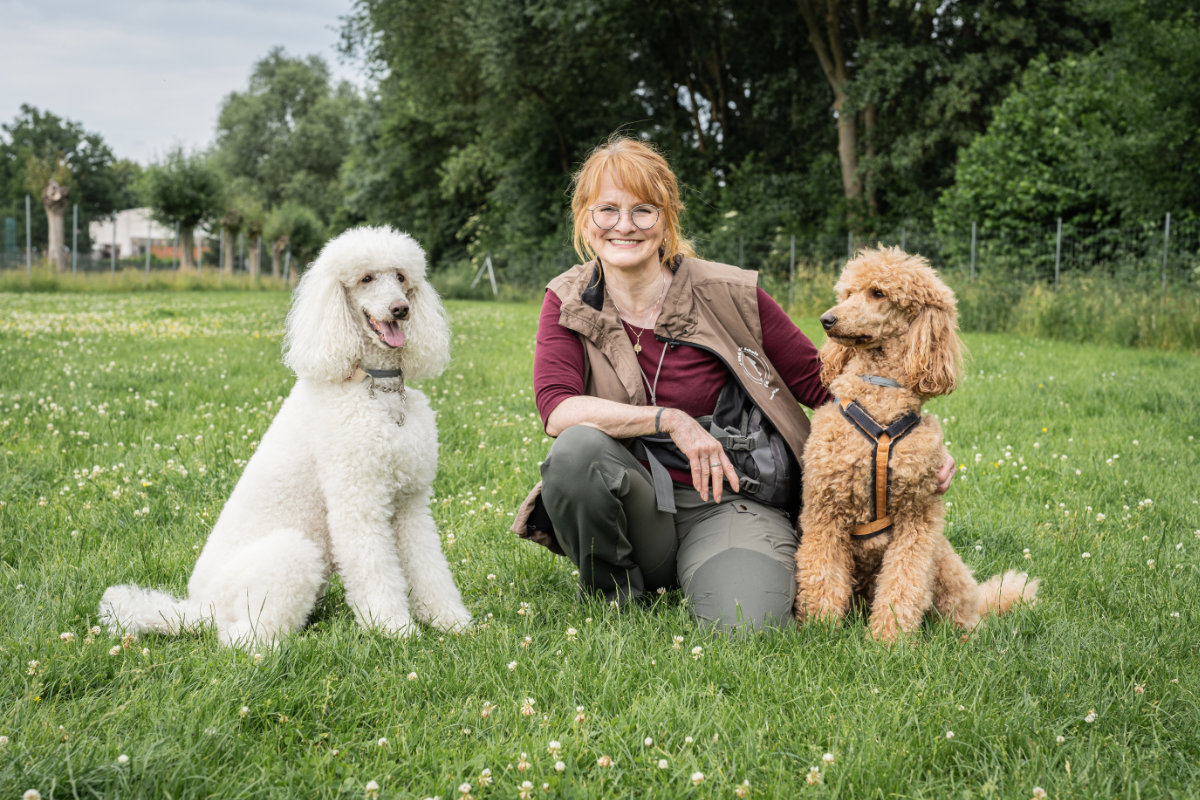 ueber-hundetrainerin-regina-gadesmann-mit-pudeln Hundetrainerin Regina Gadesmann kniet auf einer Wiese in Sibbesse zwischen ihren zwei Pudeln.